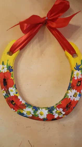Podkowa z żółtymi ramionami i barwnym kwiatowym ornamentem, przewiązana dużą czerwoną kokardą.