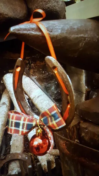 Metalowa podkowa z kokardą w kratę, czerwoną bombką i wstążką do zawieszenia.