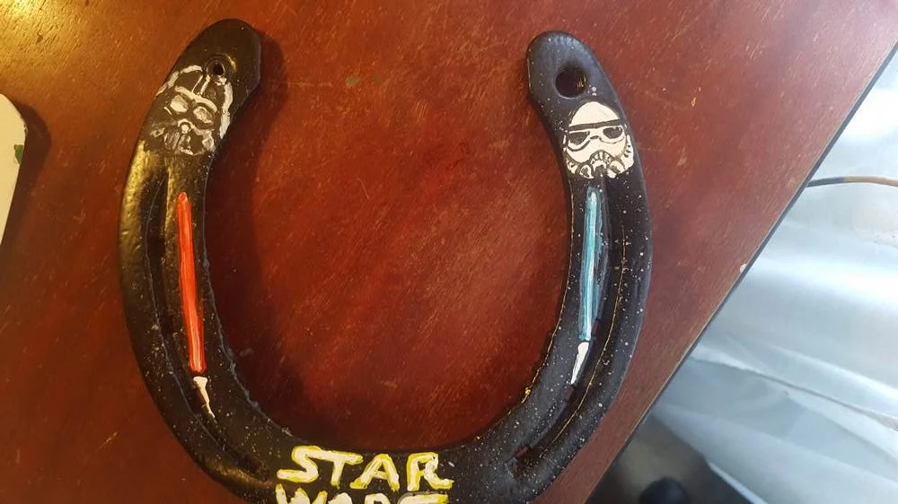 Ciemna podkowa z napisem „Star Wars”, jasnym hełmem, postacią i świetlnym mieczem.