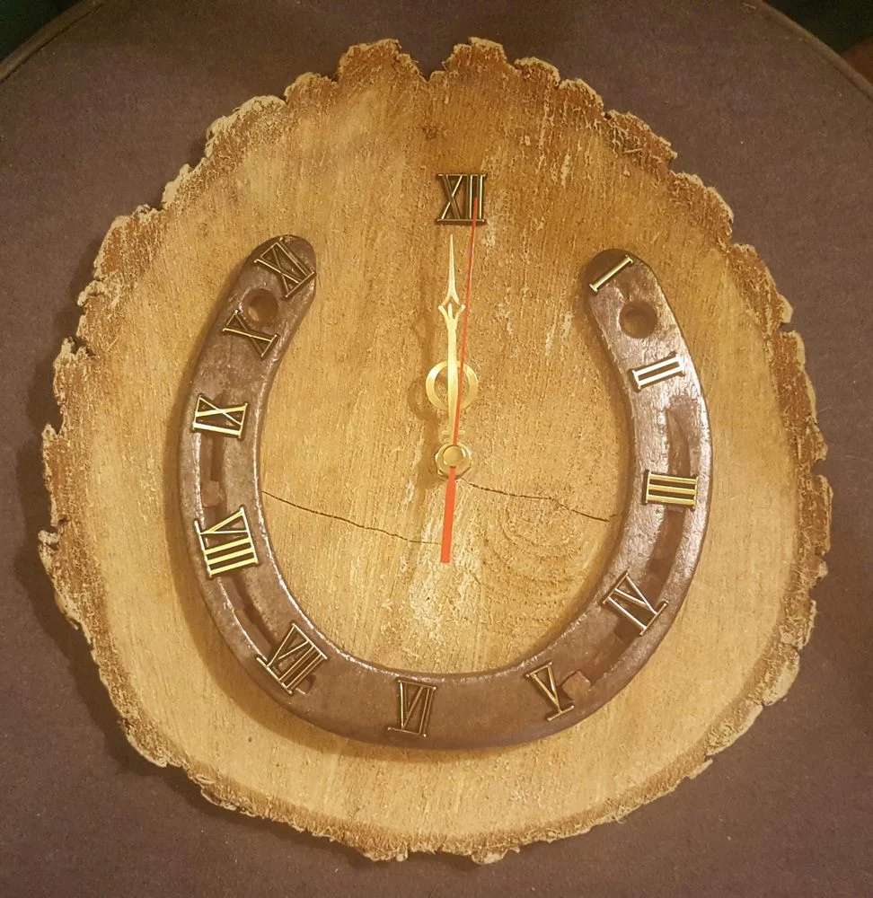Zegar z podkową, rzymskimi cyframi i złotymi wskazówkami na okrągłym plastrze drewna z korą.